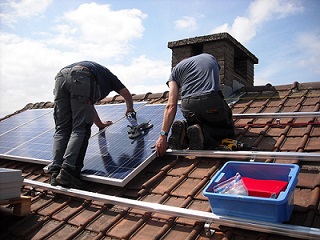 Twee mannen brengen zonnepanelen aan op een schuin dak met rode dakpannen